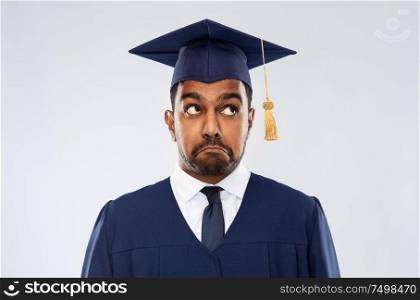 education, graduation and expression concept - confused indian male graduate student in mortar board and bachelor gown over grey background. confused indian graduate student in mortar board