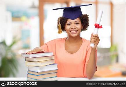 education, graduation and knowledge concept - happy smiling african american graduate student girl in bachelor hat and diploma and books over school background. african graduate student with books and diploma