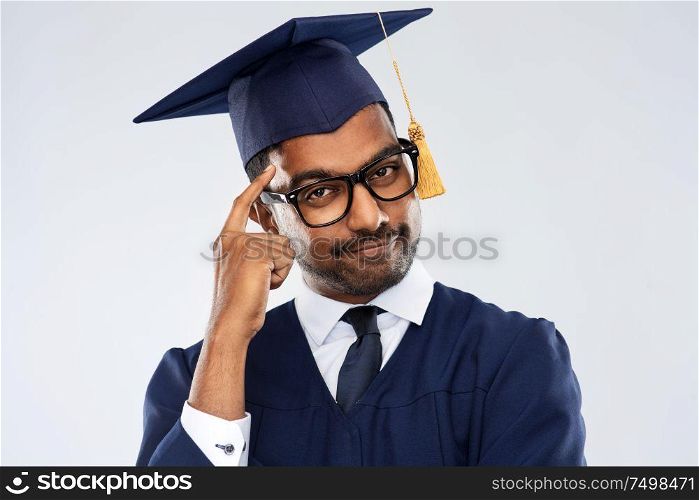education, graduation and mind concept - indian male graduate student in glasses, mortar board and bachelor gown making think gesture over grey background. indian graduate student in mortar board thinking