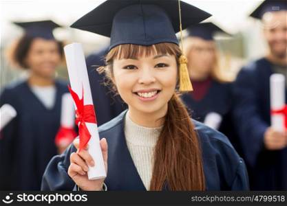 education, graduation and people concept - close up of happy student in mortar board and bachelor gown with diploma
