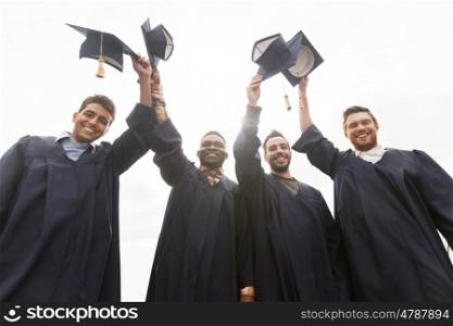 education, graduation and people concept - group of happy international male students in bachelor gowns waving mortar boards or hats