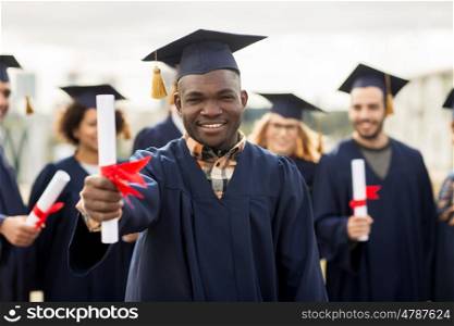 education, graduation and people concept - group of happy international students in mortar boards and bachelor gowns with diplomas