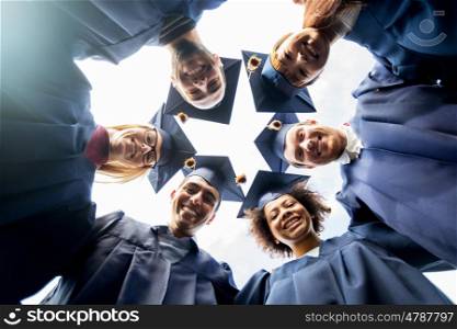 education, graduation and people concept - group of happy international students in mortar boards and bachelor gowns standing in circle