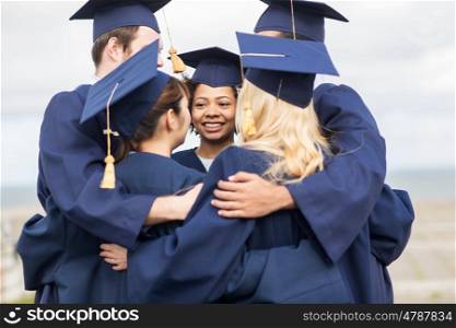 education, graduation and people concept - group of happy international students in mortar boards and bachelor gowns hugging