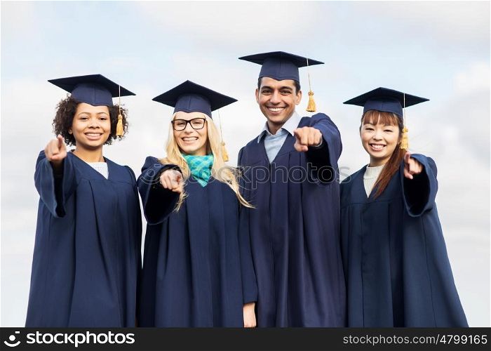 education, graduation and people concept - group of happy international students in mortar boards and bachelor gowns pointing finger at you