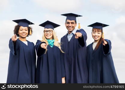 education, graduation and people concept - group of happy international students in mortar boards and bachelor gowns pointing finger at you