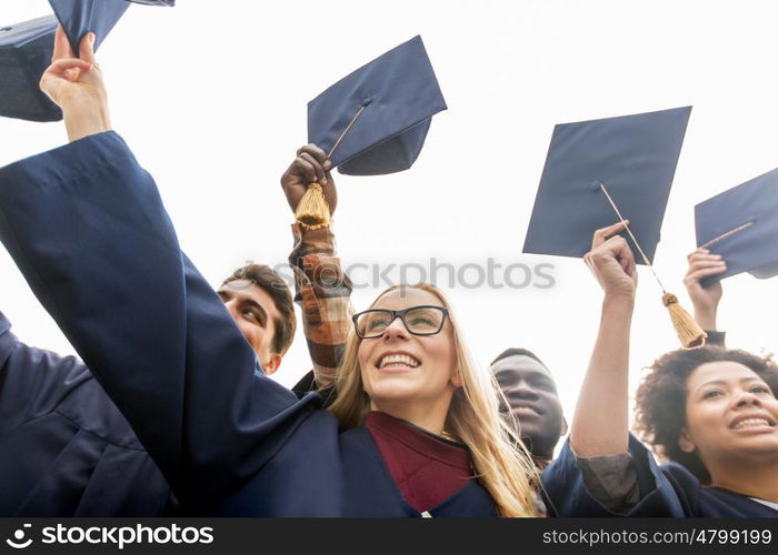 education, graduation and people concept - group of happy international students in bachelor gowns waving mortar boards or hats