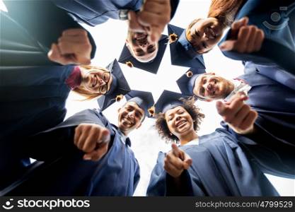 education, graduation and people concept - group of happy international students in mortar boards and bachelor gowns standing in circle and pointing finger at you