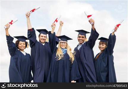 education, graduation and people concept - group of happy international students in mortar boards and bachelor gowns waving diplomas celebrating success