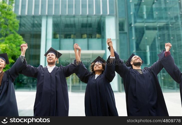 education, graduation and people concept - group of happy international students in mortar boards and bachelor gowns celebrating success over university building background