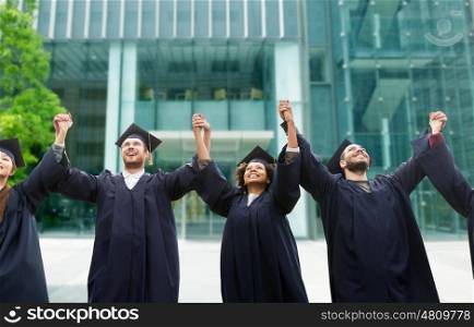 education, graduation and people concept - group of happy international students in mortar boards and bachelor gowns celebrating success over university building background