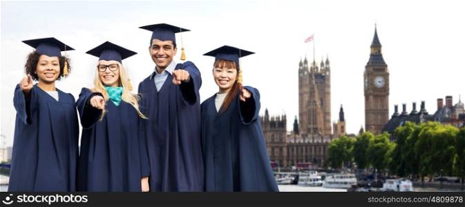 education, graduation and people concept - group of happy international students in mortar boards and bachelor gowns pointing finger at you over london city background