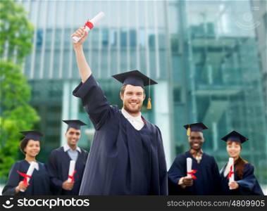 education, graduation and people concept - group of happy international students in mortar boards and bachelor gowns with diplomas over university building background