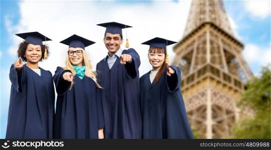 education, graduation and people concept - group of happy international students in mortar boards and bachelor gowns pointing finger at you over eiffel tower background