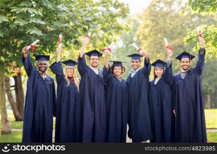 education, graduation and people concept - group of happy international students in mortar boards and bachelor gowns with diplomas celebrating success