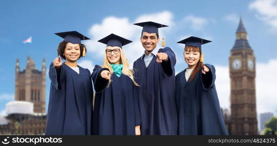education, graduation and people concept - group of happy international students in mortar boards and bachelor gowns pointing finger at you over london city background