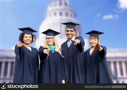 education, graduation and people concept - group of happy international students in mortar boards and bachelor gowns pointing finger at you over american white house background
