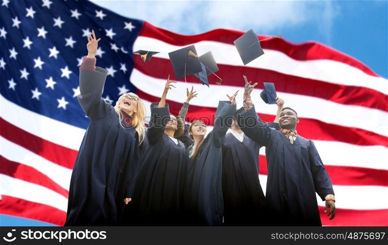 education, graduation and people concept - group of happy international students in bachelor gowns throwing mortarboards up over american flag background