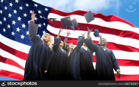 education, graduation and people concept - group of happy international students in bachelor gowns throwing mortarboards up over american flag background