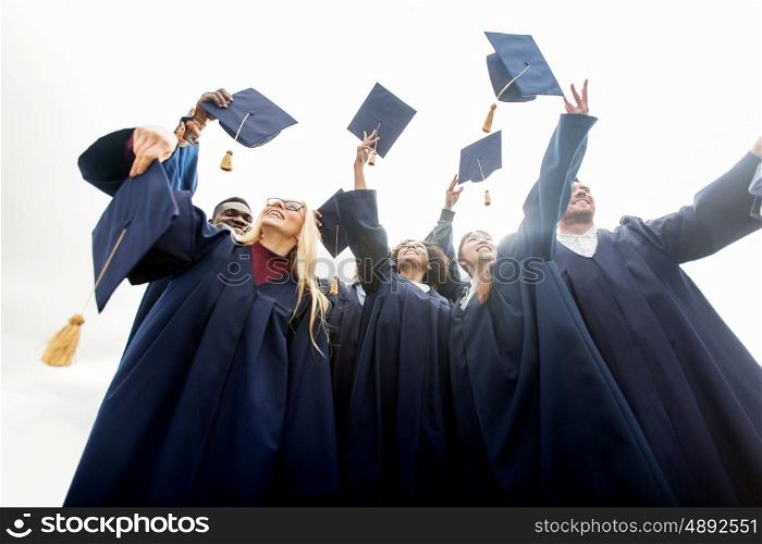 education, graduation and people concept - group of happy international students in bachelor gowns throwing mortar boards up