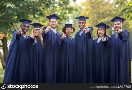education, graduation and people concept - group of happy international students in mortar boards and bachelor gowns pointing finger at you