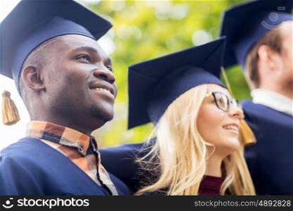 education, graduation and people concept - group of happy international students in mortar boards and bachelor gowns outdoors
