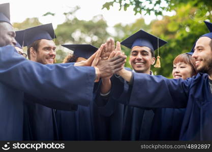 education, graduation and people concept - group of happy international students in mortar boards and bachelor gowns making high five