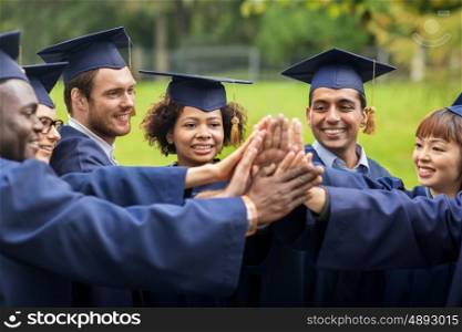 education, graduation and people concept - group of happy international students in mortar boards and bachelor gowns making high five