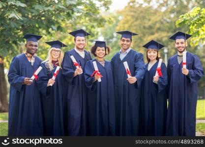 education, graduation and people concept - group of happy international students in mortar boards and bachelor gowns with diplomas