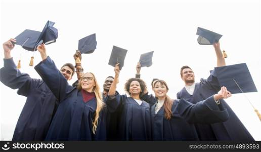 education, graduation and people concept - group of happy international students in bachelor gowns waving mortar boards or hats