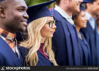 education, graduation and people concept - group of happy international students in mortar boards and bachelor gowns outdoors