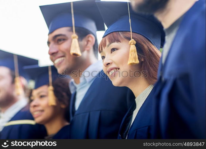 education, graduation and people concept - group of happy international students in mortar boards and bachelor gowns outdoors