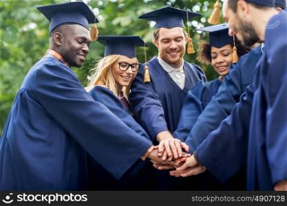 education, graduation and people concept - group of happy international students in mortar boards and bachelor gowns putting hands on top. happy students in mortar boards with hands on top