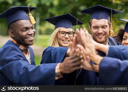 education, graduation and people concept - group of happy international students in mortar boards and bachelor gowns making high five. happy students in mortar boards making high five