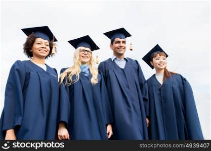 education, graduation and people concept - group of happy international students in mortarboards and bachelor gowns outdoors. happy students or bachelors in mortarboards