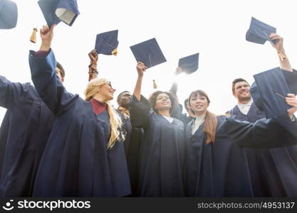 education, graduation and people concept - group of happy international students in bachelor gowns waving mortar boards or hats. happy students or bachelors waving mortar boards