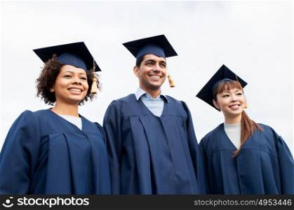 education, graduation and people concept - group of happy international students in mortarboards and bachelor gowns outdoors. happy students or bachelors in mortarboards