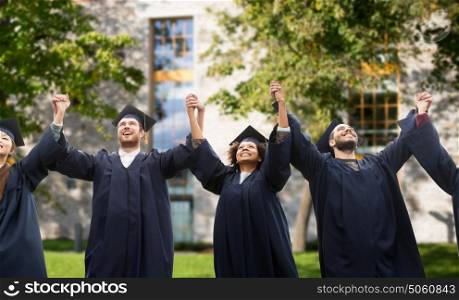 education, graduation and people concept - group of happy international students in mortar boards and bachelor gowns celebrating success over campus building background. happy students or bachelors celebrating graduation