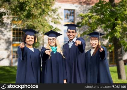 education, graduation and people concept - group of happy international students in mortar boards and bachelor gowns pointing finger at you over campus building background. happy students or bachelors pointing finger at you
