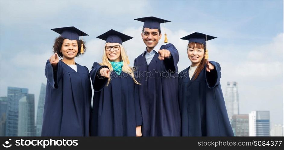 education, graduation and people concept - group of happy international students in mortar boards and bachelor gowns pointing finger at you over singapore city skyscrapers background. students or bachelors pointing at you over city. students or bachelors pointing at you over city