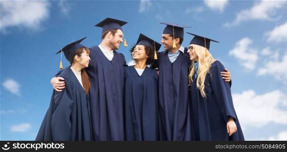 education, graduation and people concept - group of happy international students in mortar boards and bachelor gowns over blue sky and clouds background. happy students or bachelors over blue sky. happy students or bachelors over blue sky