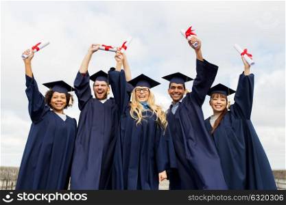 education, graduation and people concept - group of happy international students in mortar boards and bachelor gowns with diplomas celebrating success. happy students in mortar boards with diplomas