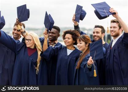 education, graduation and people concept - group of happy international students in bachelor gowns waving mortar boards. happy graduates or students waving mortar boards