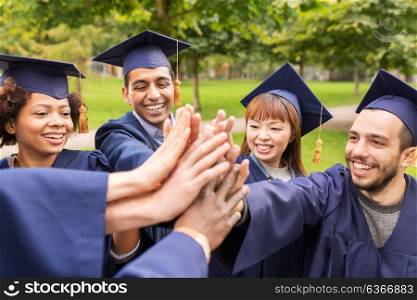 education, graduation and people concept - group of happy international students in mortar boards and bachelor gowns making high five. happy students in mortar boards making high five
