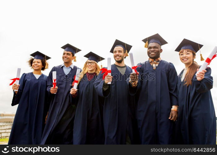 education, graduation and people concept - group of happy international students in mortar boards and bachelor gowns with diplomas. happy students in mortar boards with diplomas