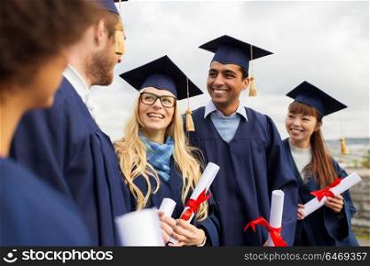 education, graduation and people concept - group of happy international students in mortar boards and bachelor gowns with diplomas. happy students in mortar boards with diplomas