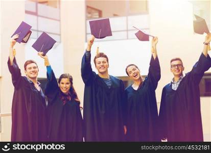 education, graduation and people concept - group of smiling students in gowns waving mortarboards outdoors