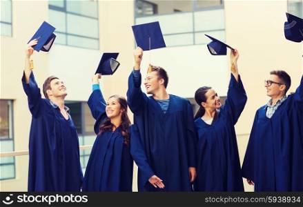 education, graduation and people concept - group of smiling students in gowns waving mortarboards outdoors