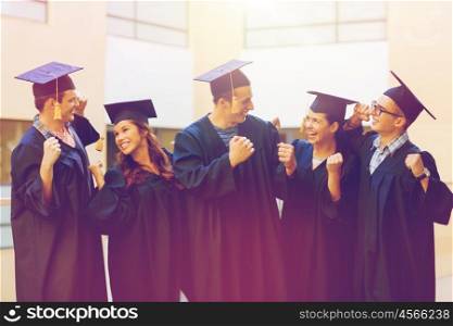 education, graduation and people concept - group of smiling students in mortarboards and gowns making triumph gesture outdoors