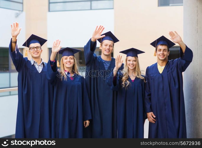 education, graduation and people concept - group of smiling students in mortarboards and gowns waving hands outdoors